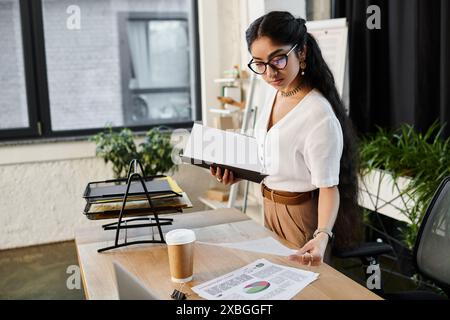 Junge indianerin mit Brille, die am Schreibtisch mit Papieren arbeitet. Stockfoto