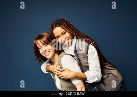 Zwei junge Frauen, die sich fröhlich in stilvoller Kleidung vor dunkelblauem Hintergrund umarmen. Stockfoto
