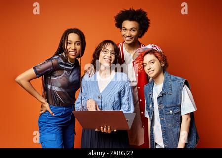 Eine vielfältige Gruppe junger Frauen, darunter auch eine nicht binäre Person, steht selbstbewusst mit einem Laptop in einem stilvollen Studio-Setting zusammen. Stockfoto