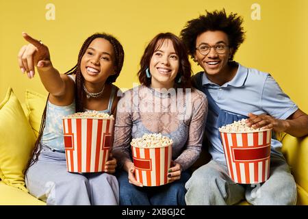 Drei Freunde genießen einen Filmabend auf einer gemütlichen Couch und halten Popcorn-Eimer in der Hand. Stockfoto