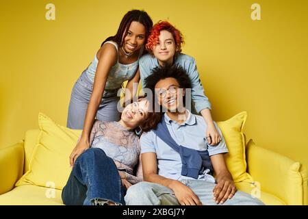 Eine Gruppe junger multikultureller Freunde, darunter eine nicht-binäre Person, die sich stilvoll auf einer gelben Couch in einem Studio-Setting entspannen. Stockfoto