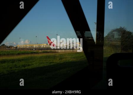 Rotes Heckflugzeug mit dem fliegenden Känguru-Logo eines QANTAS-Flugzeugs, das von einem fahrenden Bus aus über ein grasbewachsenes Feld gesehen wird, alter Flughafen brisbane, Flugdienste Stockfoto