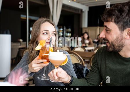 Genießen Sie in einer gemütlichen Bar ein Toast mit Cocktails. Sie lächeln und genießen ihre gemeinsame Zeit in einem stilvollen Innenbereich mit einer warmen Atmosphäre. Stockfoto