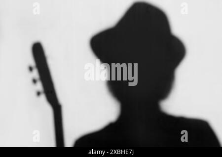 Abstrakte Personsilhouette im Hut und mit Gitarre auf grauem Hintergrund, Musikkonzept. Musiker-Silhouette spielt Akustikgitarre. Stockfoto