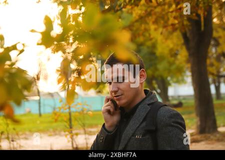 Mann, der im Herbst draußen telefoniert. Mobile Kommunikation: Mann, der in einer lockeren Herbstszene mit seinem Handy spricht. Stockfoto