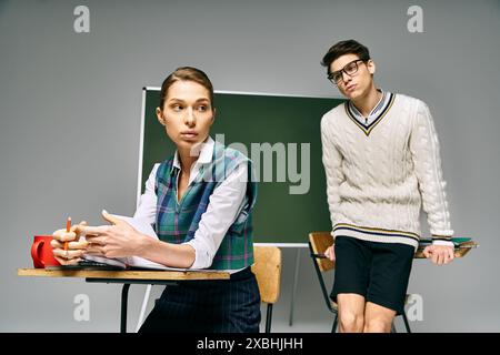Eleganter Mann und Frau im College-Setting, an einem Schreibtisch vor einer grünen Tafel. Stockfoto