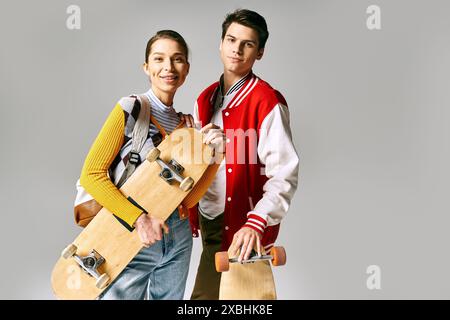 Zwei junge Menschen halten Skateboards selbstbewusst vor grauem Hintergrund. Stockfoto