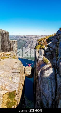 Eine Person steht am Rande des Kjeragbolten Kanzel Rock in Norwegen und blickt auf die atemberaubende Landschaft darunter. Asiatische Frauen in Kjeragbolten Stockfoto