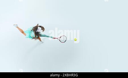 Dynamische Luftaufnahme einer jungen, athletischen Tennisspielerin, die vor weißem Studiohintergrund einen Vorschuss trifft. Stockfoto