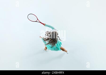 Draufsicht von einer sportlichen Frau in mintgrünem Tennisoutfit, die Serve vor weißem Studiohintergrund ausführt. Stockfoto