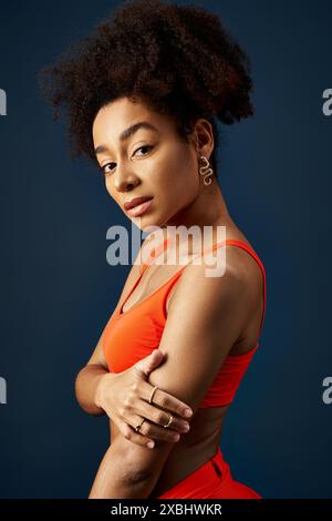 Stilvolle junge afroamerikanische Frau posiert selbstbewusst in farbenfrohem orangefarbenen Oberteil. Stockfoto