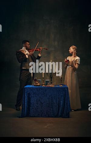 Renaissance-Musik. Schöner afroamerikanischer Adliger, der Geige für elegante junge Frau vor Vintage-Muster spielt Stockfoto