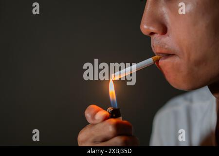 Nahaufnahme einer Person, die eine Zigarette mit einem Feuerzeug anzündet. Der Hintergrund ist dunkel und der Fokus liegt auf der Zigarette und der Flamme. Stockfoto