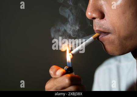 Nahaufnahme einer Person, die eine Zigarette mit einem Feuerzeug anzündet, mit sichtbarem Rauch. Stockfoto