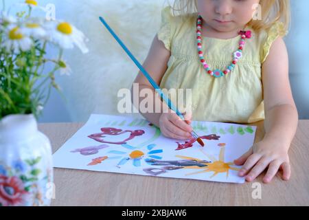 Kleines Kind, kleines Mädchen im Vorschulalter 3 Jahre malt mit Pinsel helles Bild auf Papier, kindliche naive Zeichnung in farbigen Aquarellen, Gouache, Acryl Stockfoto