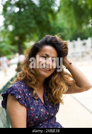 Porträt einer schönen hispanischen Frau, die in die Kamera lächelt, während sie in einem Park in Paris sitzt Stockfoto