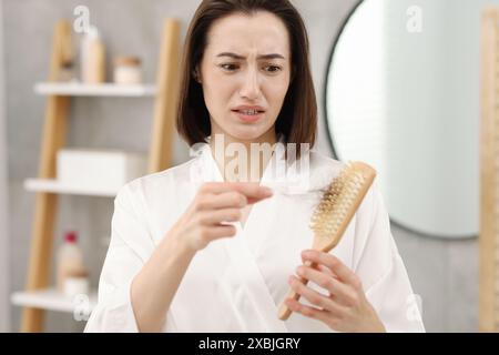 Eine gestresste Frau nimmt ihr verlorenes Haar aus der Bürste im Badezimmer. Alopezie-Problem Stockfoto