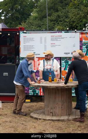 Festivalbesucher, die beim Red Rooster Musikfestival Euston Hall Suffolk England mit den Preislisten auf dem Kabeltisch mit Feuerball entspannen Stockfoto