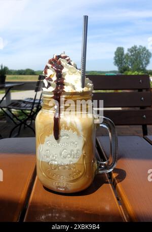 Ein köstlicher Eiskaffee mit Schlagsahne und Schokoladensirup, serviert in einem maurerglas auf einer sonnigen Terrasse im Freien. Stockfoto
