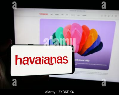 Person mit Smartphone und Logo des brasilianischen Flipflop-Herstellers Havaianas vor der Website. Schwerpunkt auf dem Display des Telefons. Stockfoto