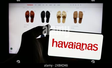 Person, die ein Mobiltelefon mit dem Logo des brasilianischen Flipflop-Herstellers Havaianas vor der Webseite hält. Schwerpunkt auf dem Display des Telefons. Stockfoto