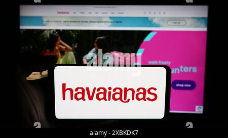 Person, die ein Handy mit dem Logo des brasilianischen Flipflop-Herstellers Havaianas vor der Business-Webseite hält. Schwerpunkt auf dem Display des Telefons. Stockfoto