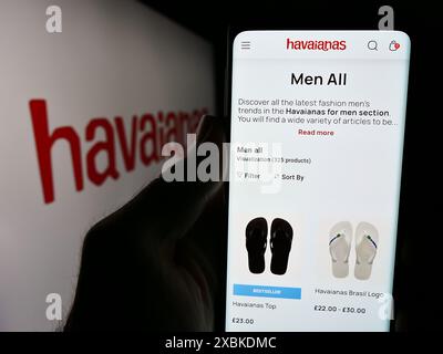 Person mit Handy und Website der brasilianischen Flipflop-Herstellerfirma Havaianas vor dem Logo. Konzentrieren Sie sich auf die Mitte des Telefondisplays. Stockfoto