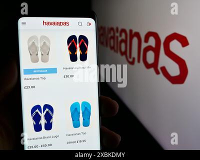 Person mit Smartphone und Webseite des brasilianischen Flipflop-Herstellers Havaianas vor dem Logo. Konzentrieren Sie sich auf die Mitte des Telefondisplays. Stockfoto