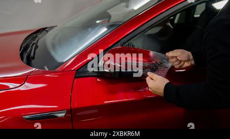 Der Master trägt Vinylfolie auf den Seitenspiegel eines Autos auf. Stockfoto