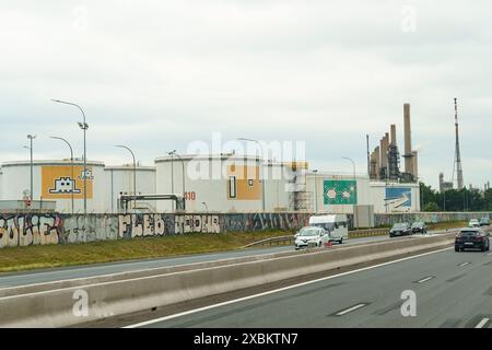 Lyon, Frankreich - 16. Mai 2023: Neben einer befahrenen Autobahn ist eine Industrieanlage mit Lagertanks mit Graffiti zu sehen, im Hintergrund Smok Stockfoto