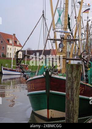 Segelboote im Hafen mit reflektierendem Wasser, Masten und Seilen an einem bewölkten Tag, greetsiel, ostfriesland, deutschland Stockfoto