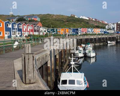 Boote, die auf einem Holzsteg vor einer Reihe von bunten Häusern ankern, Helgoland, Nordsee, Deutschland Stockfoto