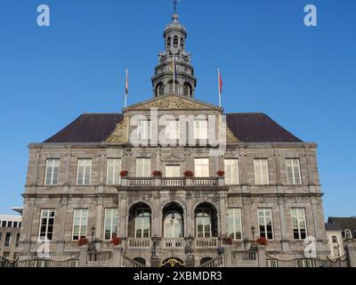 Historisches Rathaus mit Steinfassade und Fahnen vor klarem blauem Himmel, Maastricht, limburg, niederlande Stockfoto