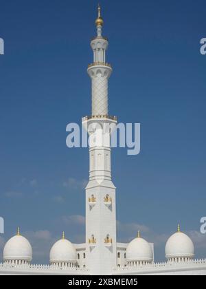 Hohes Minarett mit raffinierten Details, flankiert von Kuppeln unter blauem Himmel, abu dhabi, vereinigte arabische emirate Stockfoto