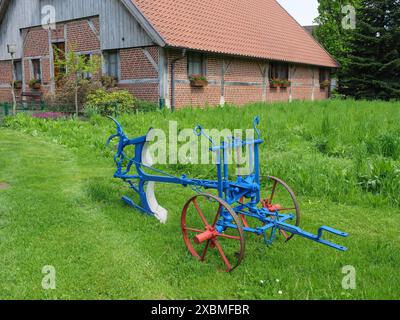 Moderne blaue und rote Landwirtschaftsgeräte in einem grünen Garten vor einem traditionellen Haus, Marbeck, westfalen Stockfoto