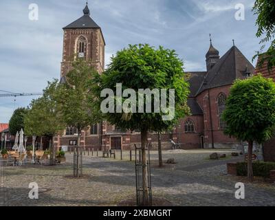 Kirche mit hohem Turm auf einem kleinen, gepflasterten Platz mit Bäumen und Straßenlaternen unter bewölktem Himmel, Ramsdorf, münsterland, Deutschland Stockfoto