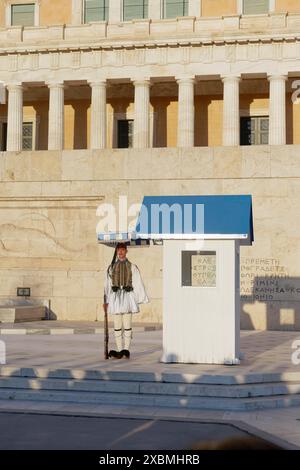 Evzone in traditioneller Kleidung steht neben einer Wachhütte unter einem Sonnenschirm, dem Parlamentsgebäude, dem Grab des unbekannten Soldaten, dem Syntagma-Platz, Athen Stockfoto