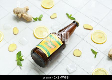 Komposition mit Flasche frisches Ingwerbier, Minze, Zitronenscheiben und Eiswürfeln auf hellem Fliesenhintergrund, Nahaufnahme Stockfoto