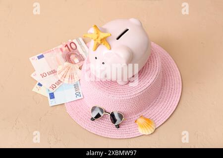 Schweinebank mit Strandaccessoires und Geld auf beigem Hintergrund. Konzept der Reisekostenersparnis Stockfoto