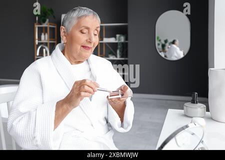 Eine ältere Frau, die sich im Badezimmer schminkt Stockfoto