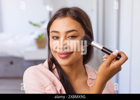 Glückliche Frau, die Make-up mit Pinsel aufträgt und warm lächelt Stockfoto