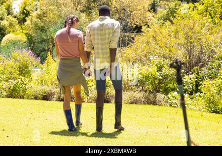 Glückliches, vielseitiges Paar, das Hände hält, im Garten spaziert Stockfoto