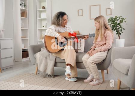 Reife Frau mit ihrer kleinen Enkelin, die zu Hause Geschenkgitarre spielt Stockfoto