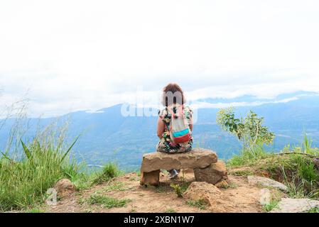 Nicht erkennbare Frau von hinten gesehen auf einer Steinbank sitzend, ruhend und genießt einen spektakulären Blick auf die Berglandschaft in einer natürlichen Gegend ne Stockfoto