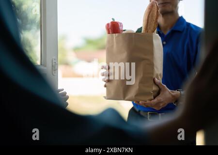 Person, die Lebensmittel an die Haustür liefert, kontaktloser Lieferservice, sichere und bequeme Lieferung nach Hause, frische Lebensmittel in Papiertüte Stockfoto