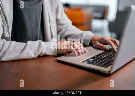 Ein Nahbild eines asiatischen Mannes in bequemer Kleidung, der an seinem Laptop arbeitet, auf der Tastatur des Laptops tippt, drinnen an einem Tisch arbeitet. Stockfoto