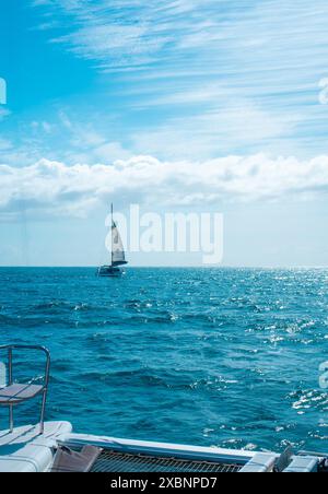 Ein Segelboot gleitet über den ruhigen blauen Ozean unter einem klaren Himmel mit flauschigen weißen Wolken. Stockfoto