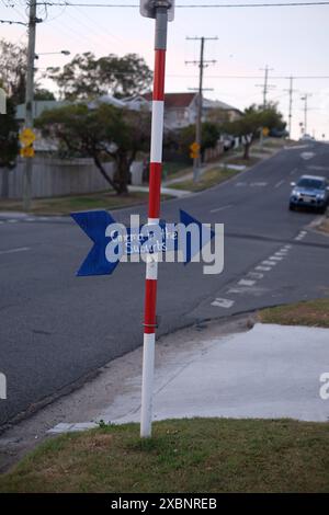 Ein handgefertigtes Schild, ein blau bemalter Pfeil mit der Inschrift Cinema in the Suburbs, befestigt an einem rot-weiß gestreiften Schulkreuzmast in Carina, Brisbane Stockfoto