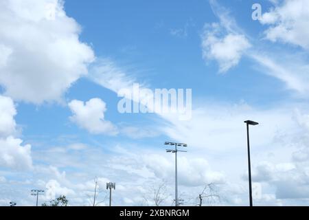 Die Spitzen von Lichtmasten, Stangen und einem Funkgerät ragen vor einem Himmel, weiße Cumulus-Wolken und Blöcke für den klaren blauen Himmel über einem Parkplatz in Brisbane, Australien Stockfoto