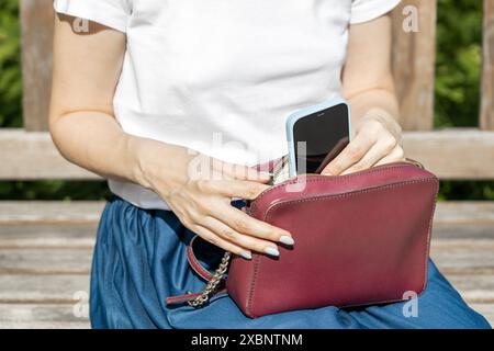 Frau nimmt das Smartphone aus der Handtasche, Nahaufnahme. Das Mädchen steckt ihr Handy in die Tasche. Hochwertige Fotos Stockfoto